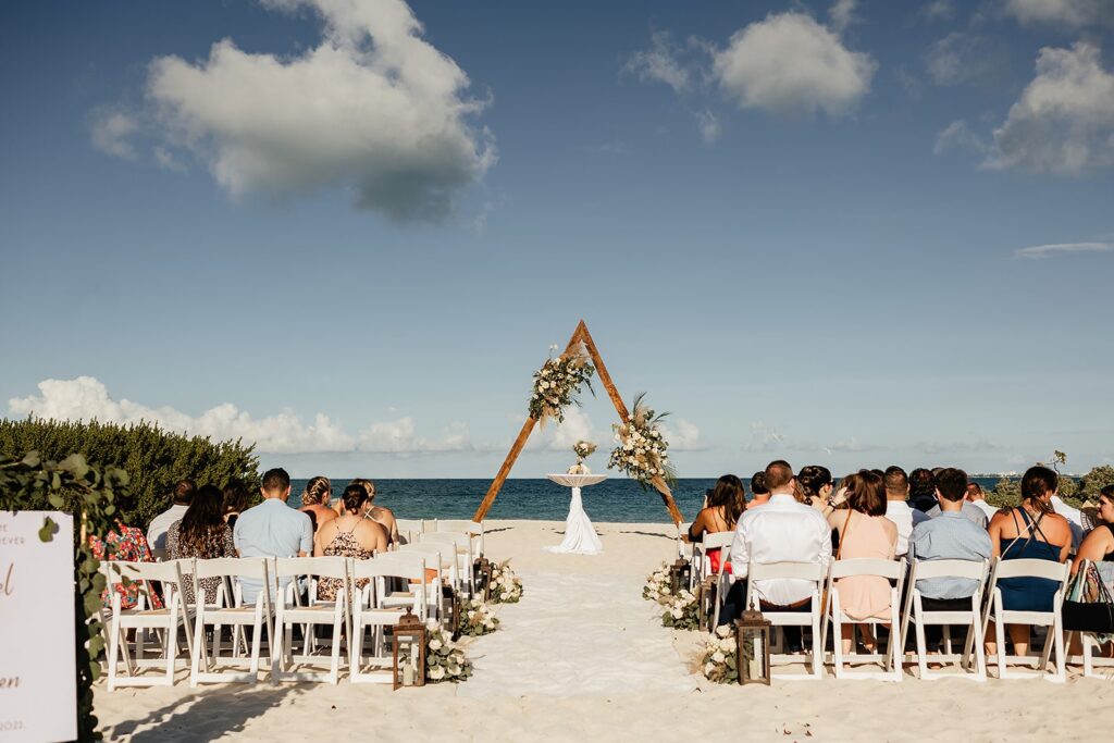 Planning a destination wedding: guests sit on white chair on the beach waiting for the destination wedding ceremony to start