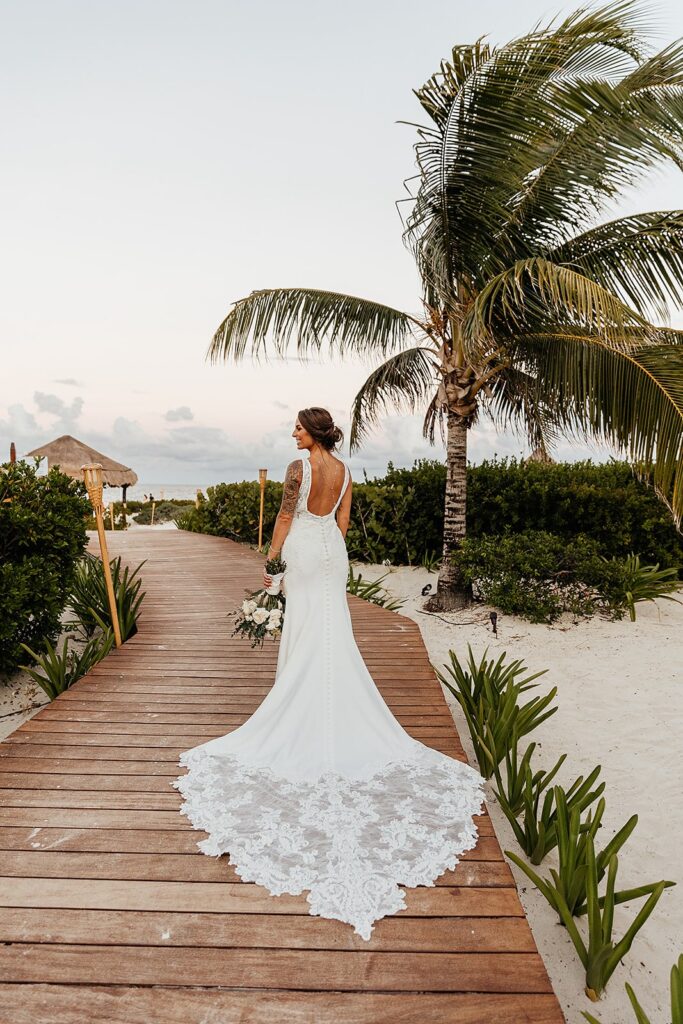 Bride walks along a wood boardwalk on the beach during her destination wedding in Mexico