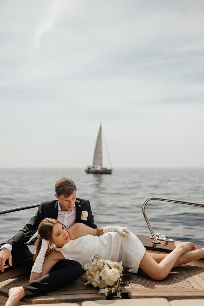 Bride lays next to groom on the deck of a private boat at their East Coast wedding venue
