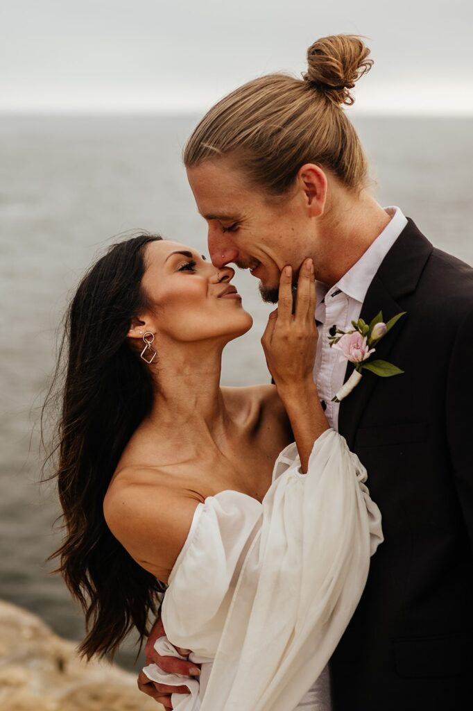 Bride and groom kiss on the coast at their East Coast wedding