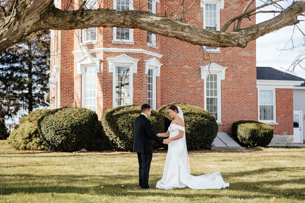 Bride and groom hold hands during their East Coast wedding in front of a brick house