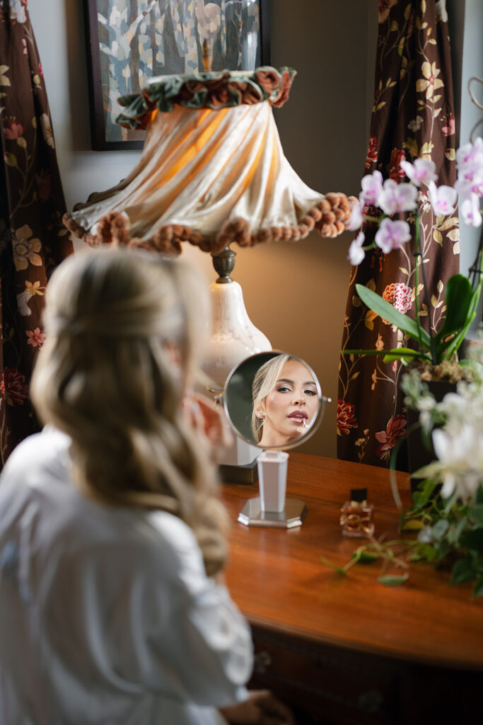 Bride applying lipstick in the mirror as she gets ready