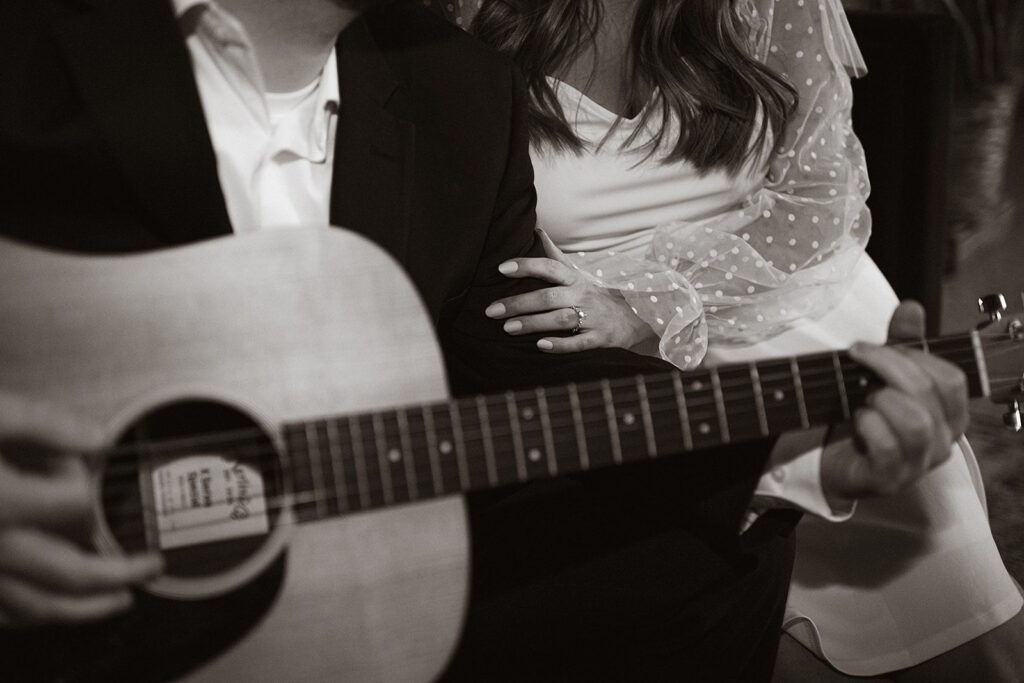 Man plays the guitar for his fiancee during their hotel engagement photo session