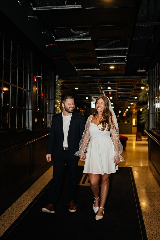 Couple holds hands while walking through the halls at Bottleworks Hotel during their engagement photo session