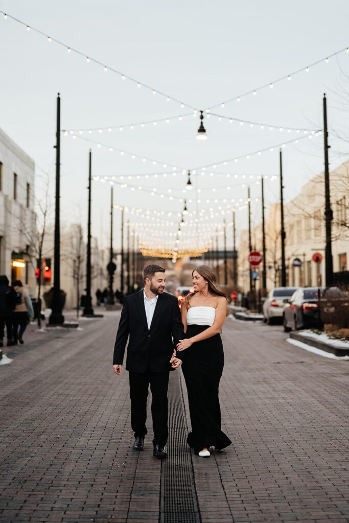 Couple holds hands while walking through downtown Indianapolis for their engagement photo session