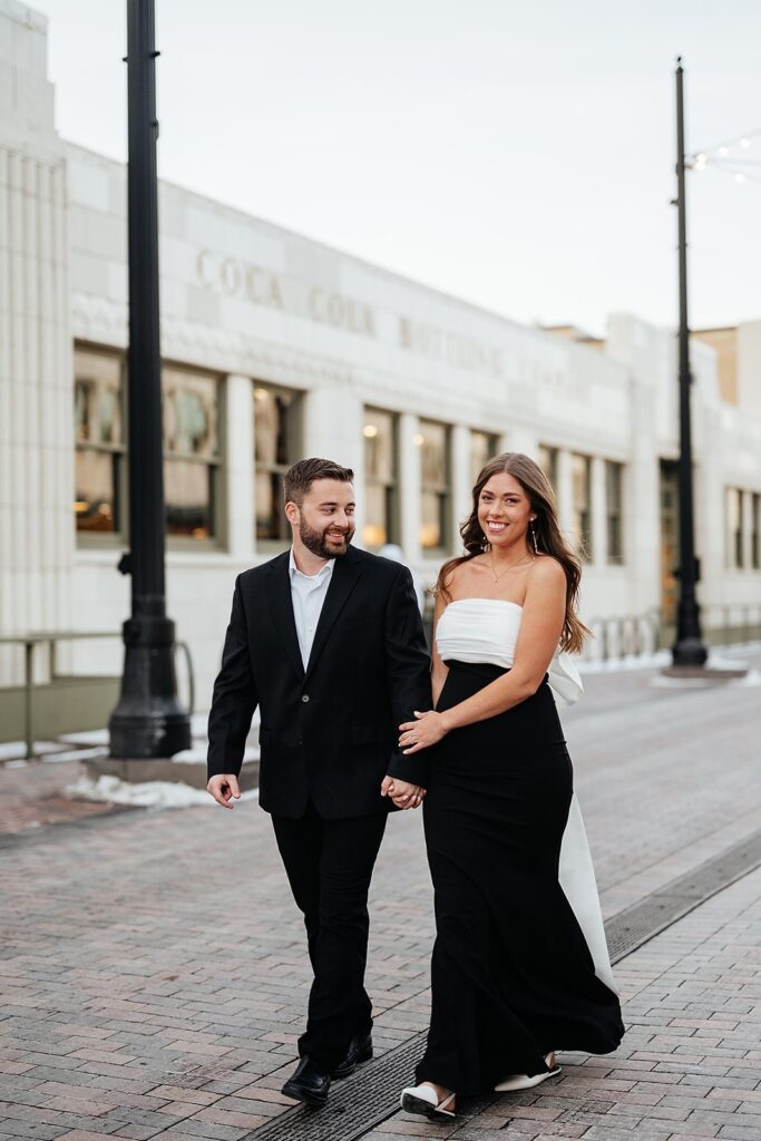 Couple holds hands while walking through downtown Indianapolis for their engagement photo session