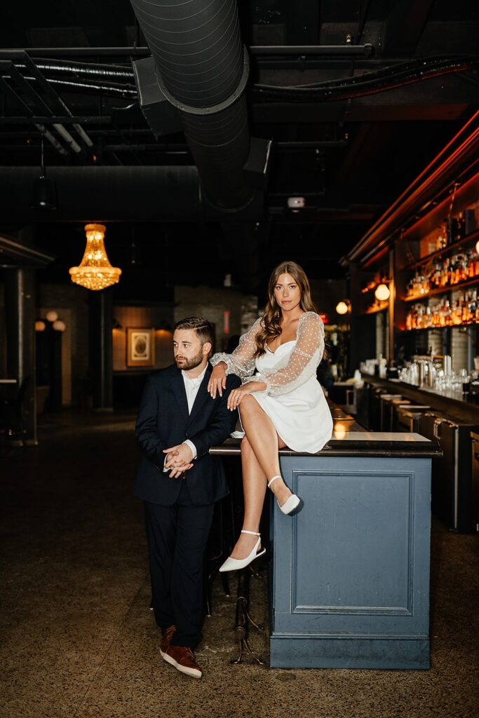 Woman sits on the bartop at a hotel bar during their hotel engagement photos