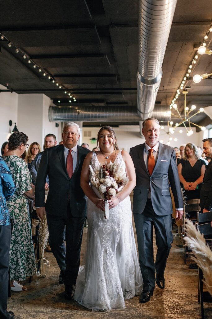 Bride walks down the aisle with two fathers at her Fort Wayne wedding at the Paper Mill