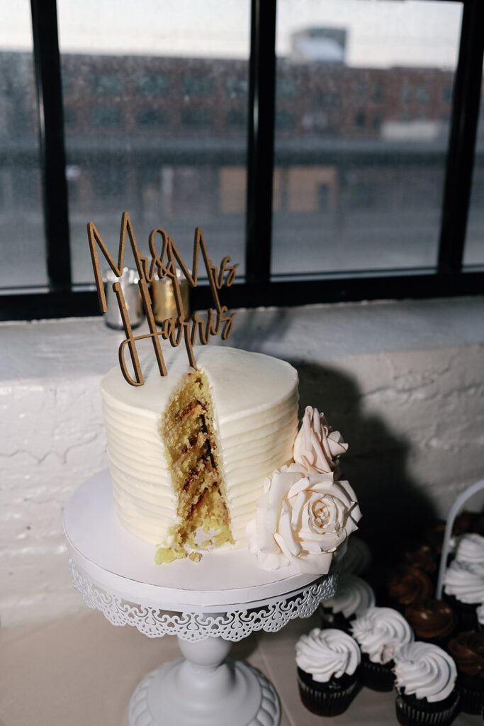 White wedding cake with custom wood topper that reads "Mr & Mrs Harris"