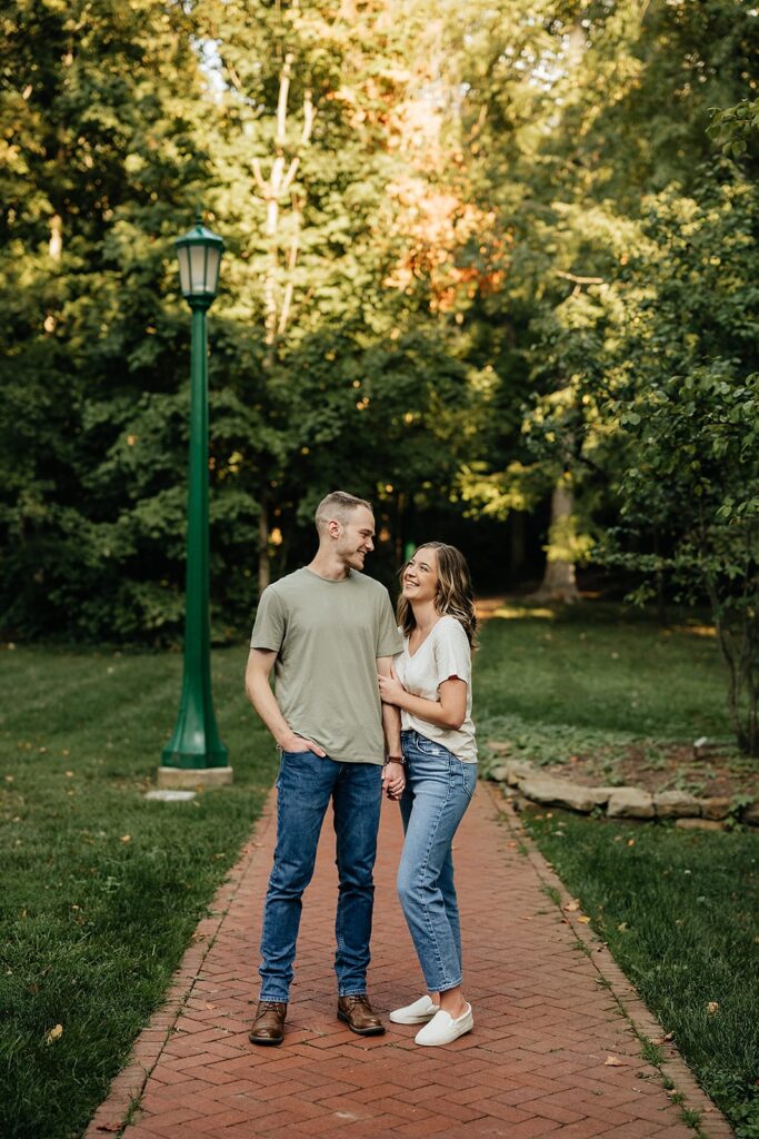 Couple stands on brick sidewalk holding hands during their Indiana University engagement photos