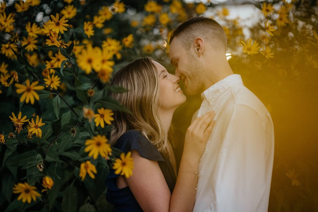 Man and woman kiss in front of yellow flowers during their engagement photo session at Indiana University