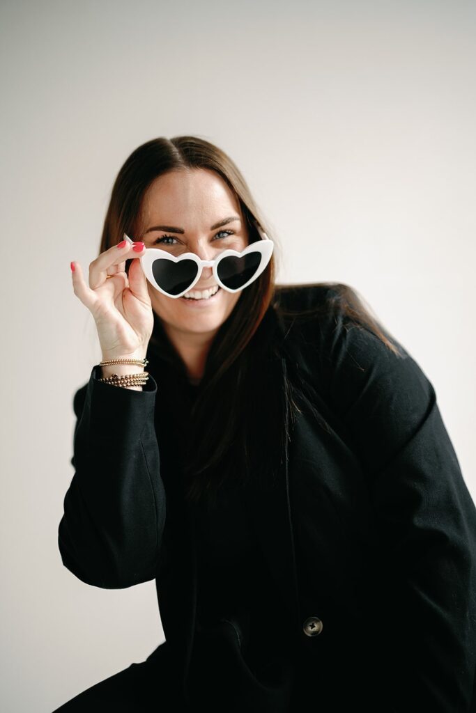 Wedding content creator wearing black pant suit and white heart sunglasses in a studio