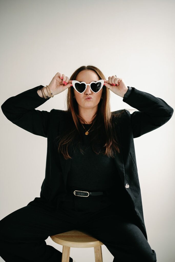 Wedding content creator wearing black pant suit and white heart sunglasses in a studio