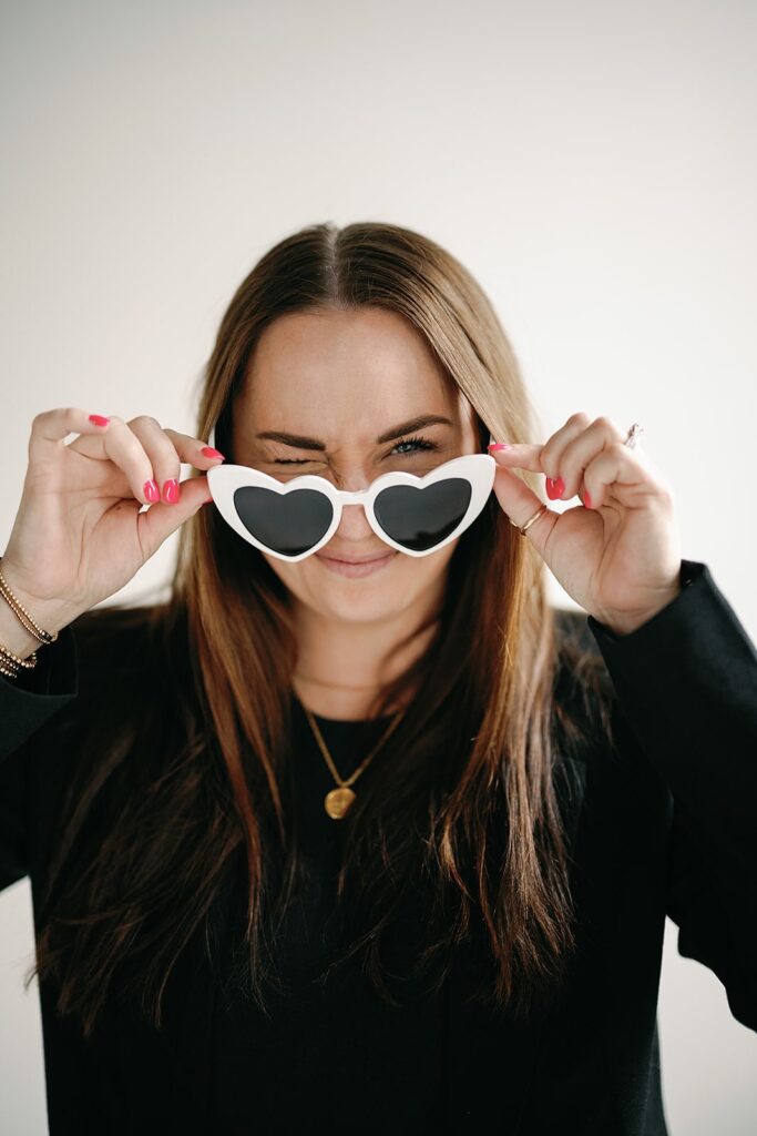 Wedding content creator wearing black pant suit and white heart sunglasses in a studio