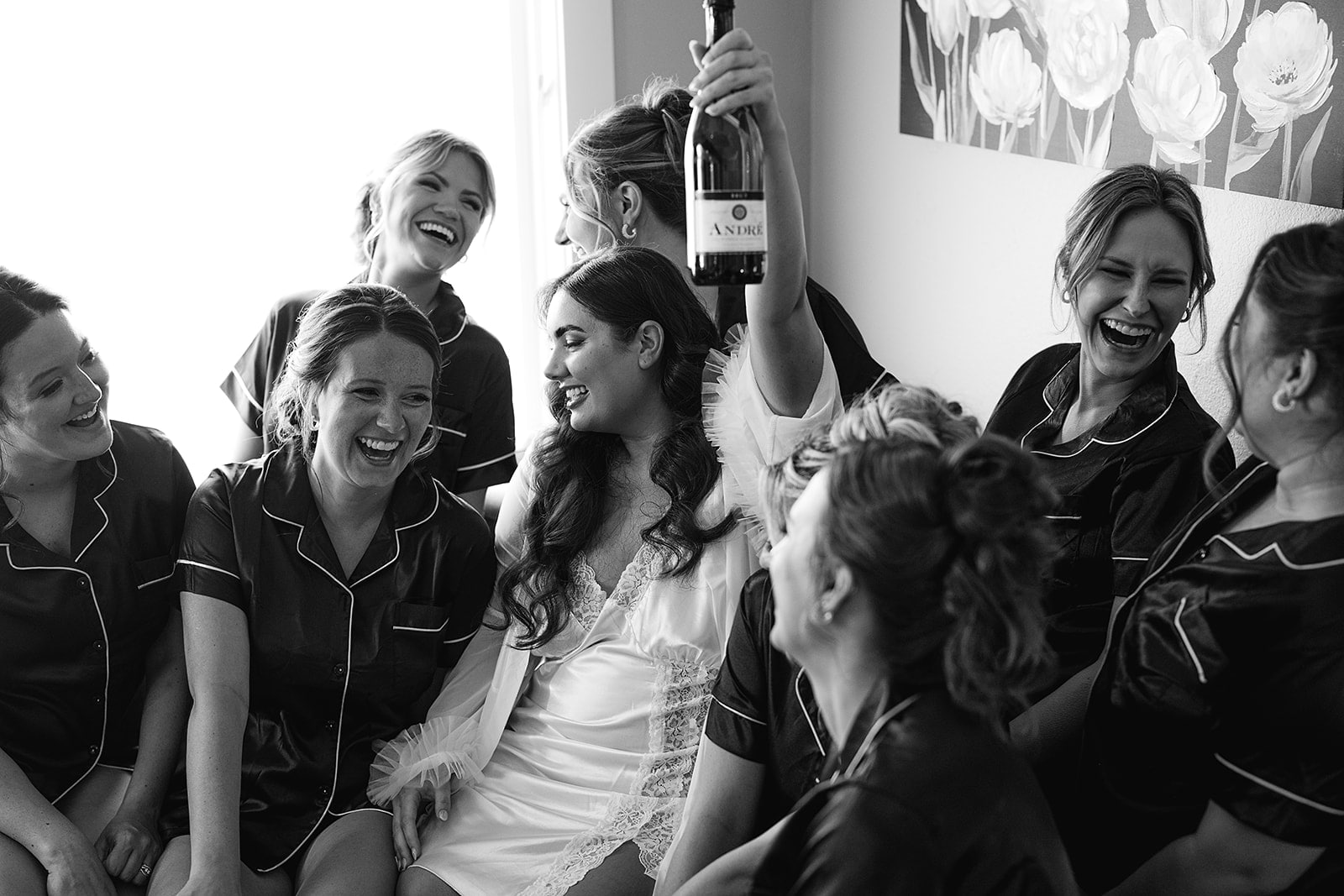 Bride lifts a bottle of champagne into the air while getting ready with her wedding party