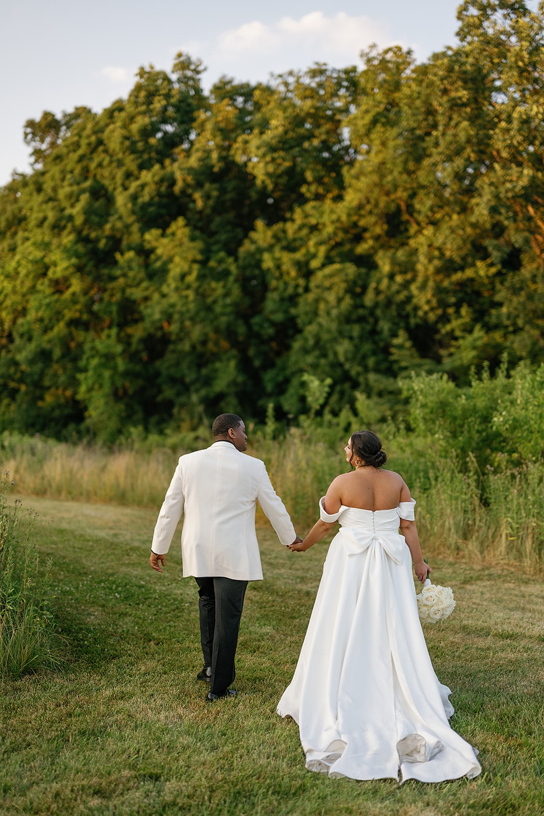 Bride and groom hold hands as they walk through a field during their Midwest wedding photos in Indiana