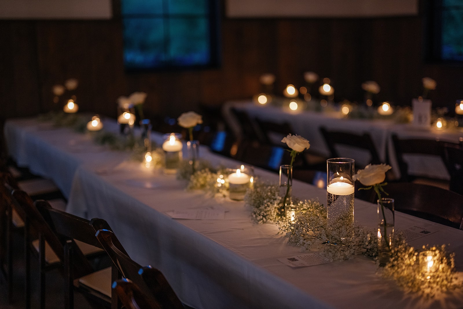 Candles and baby's breath flowers line the middle of a whit and black wedding reception table