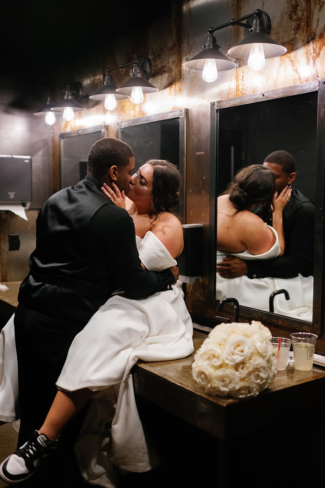 Bride and groom sit on a bathroom counter at Union 12 kissing during their Midwest wedding