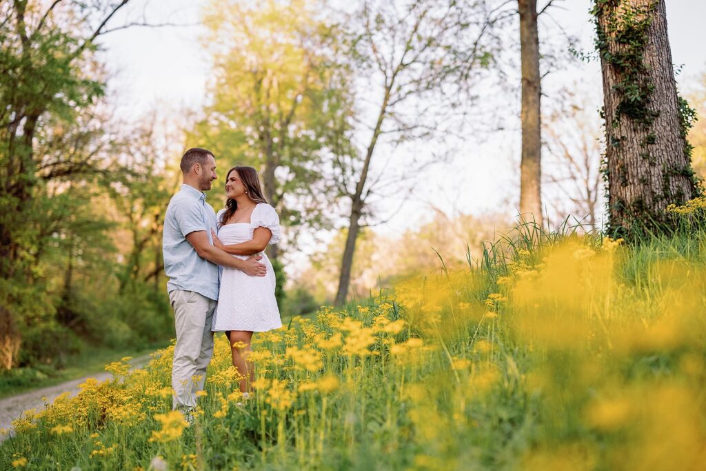 Man and woman hug in a golden wildflower field during their engagement photos