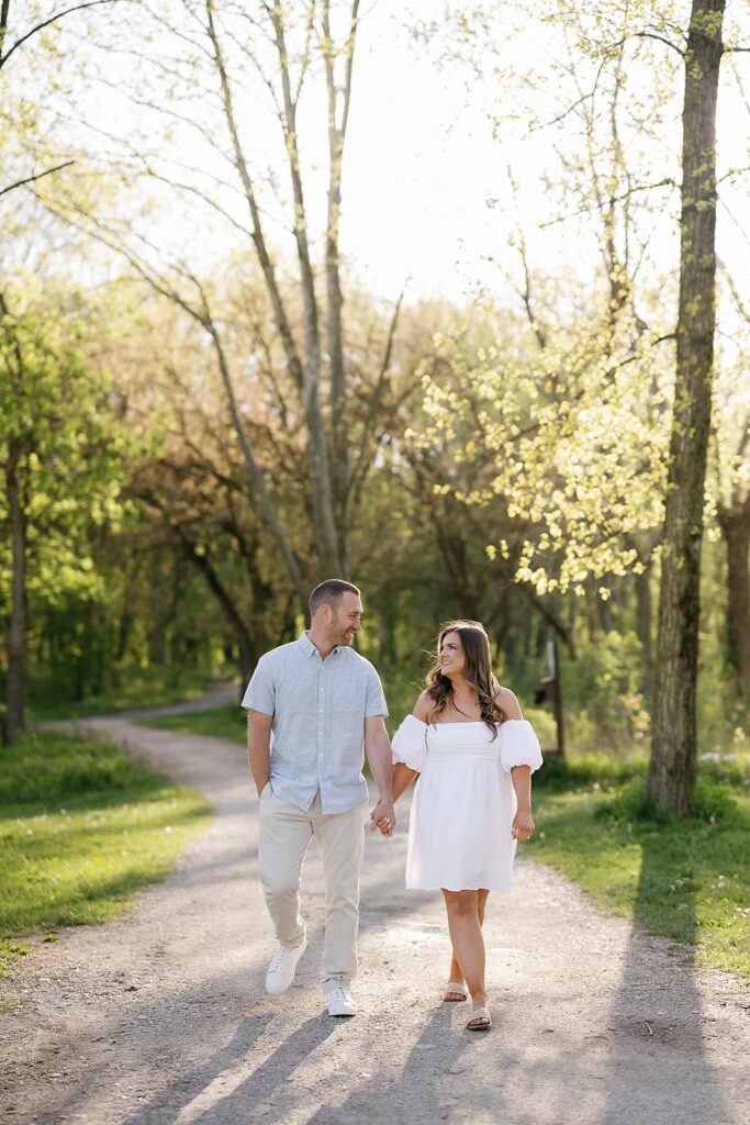 Couple holds hands while walking down a wooded trail during their Newfields engagement session