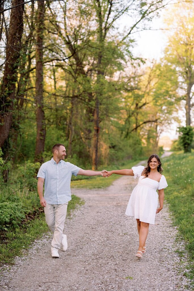 Man and woman hold hands while walking down a gravel trail during their engagement session at Newfields