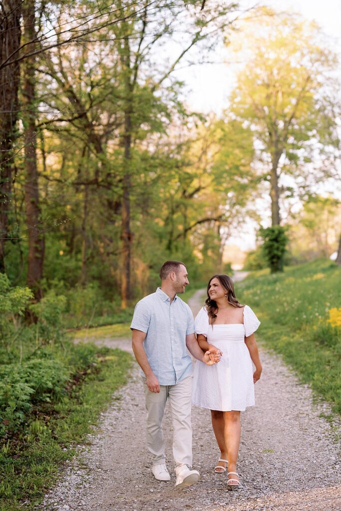 Couple holds hands while walking down a gravel trail during their Newfields engagement session