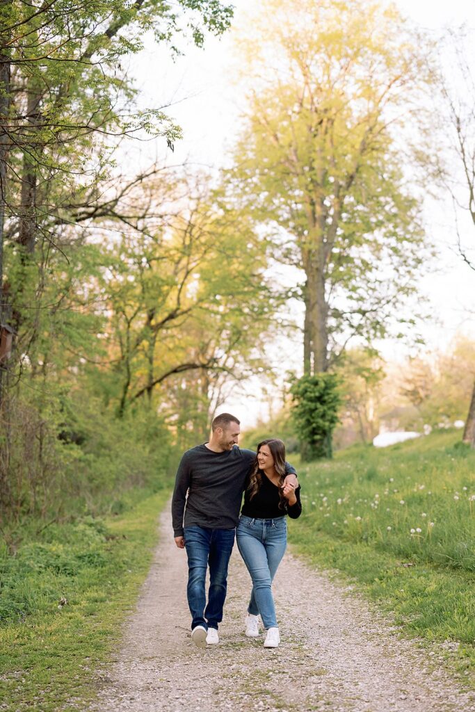 Couple hugs and laughs while walking down a gravel trail during their engagement photos at Newfields