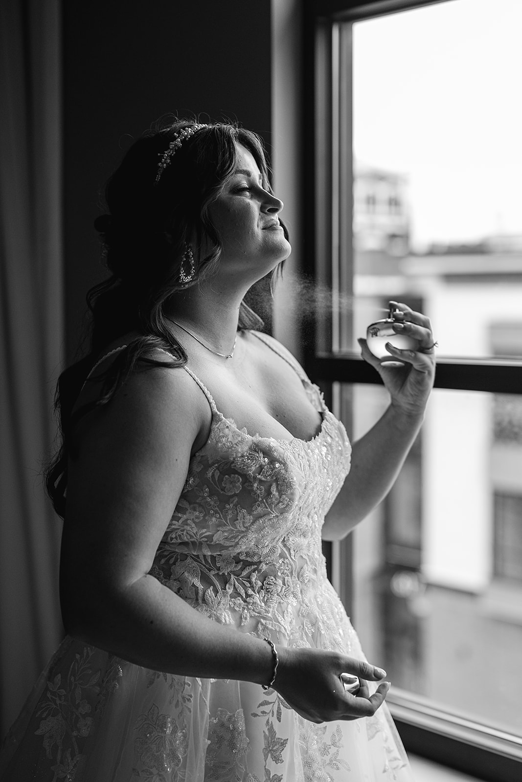 Black and white photo of a bride spritzing perfume on as she gets ready