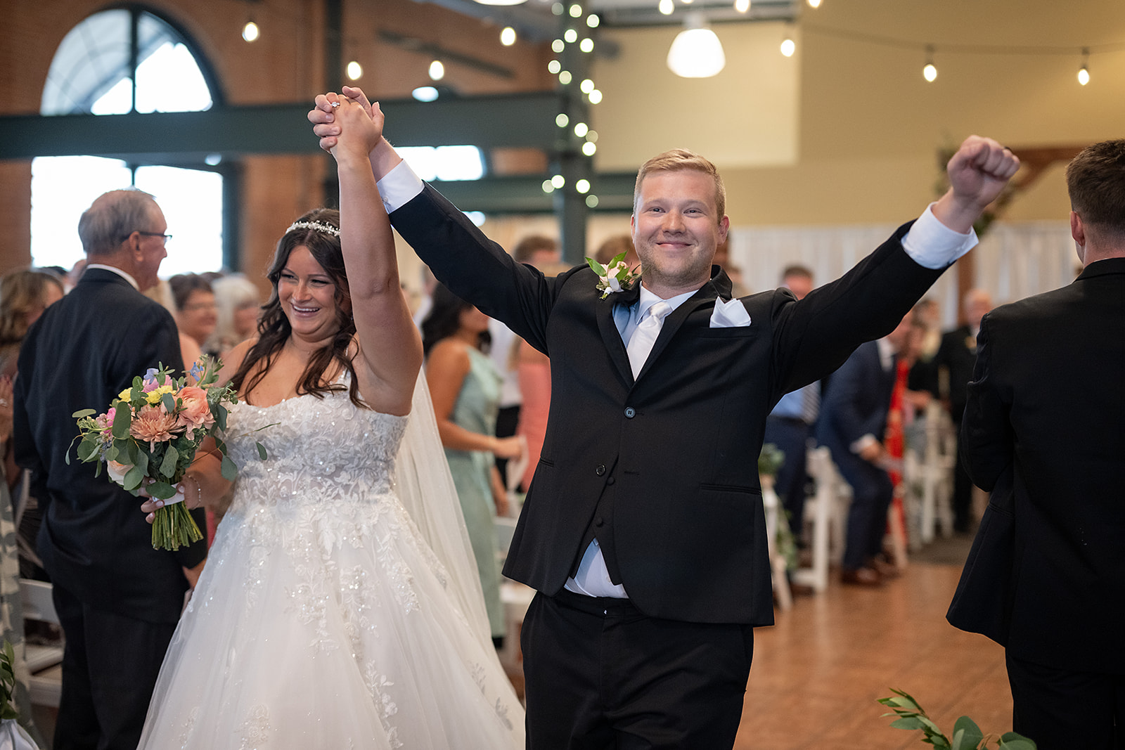 Bride and groom celebrating as they walk towards the end of the aisle after their ceremony