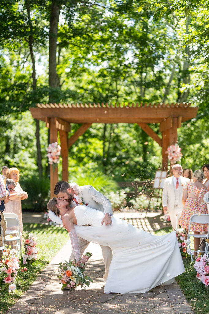 Bride and grooms end of aisle dip kiss during their outdoor Stone Creek Lodge wedding ceremony