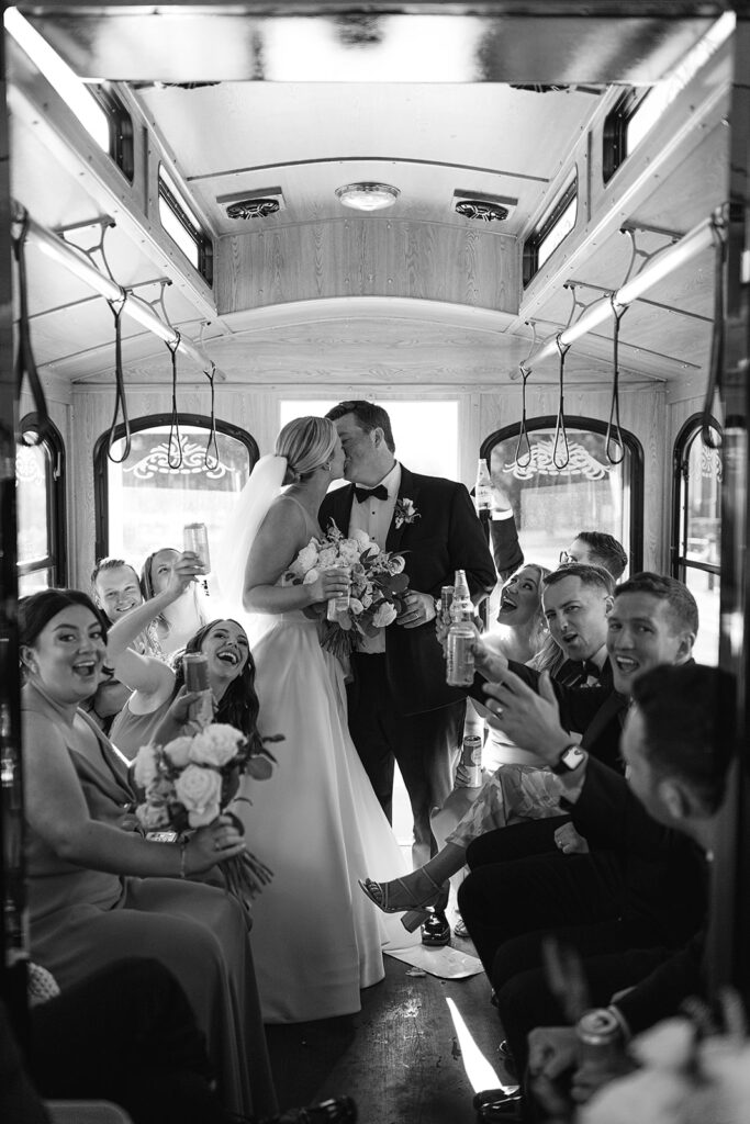 Bride and groom kissing on the trolley with their wedding party