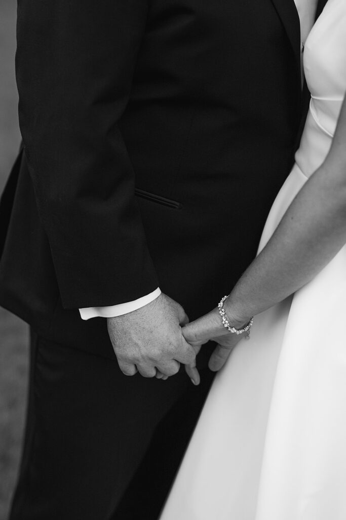 Black and white close up shot of a bride and groom holding hands