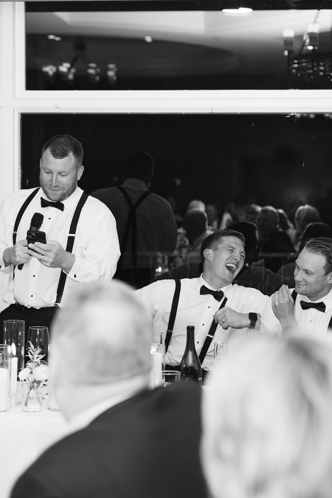 Candid black and white wedding reception photo of guests laughing during speeches