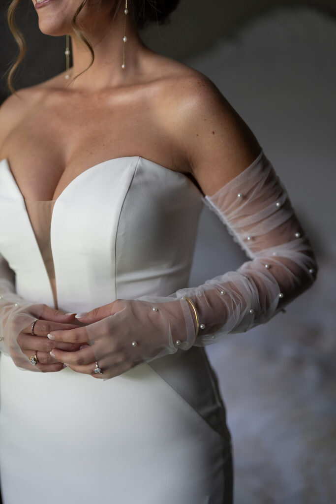 Close up shot of a bride wearing her dress with pearl studded sleeves