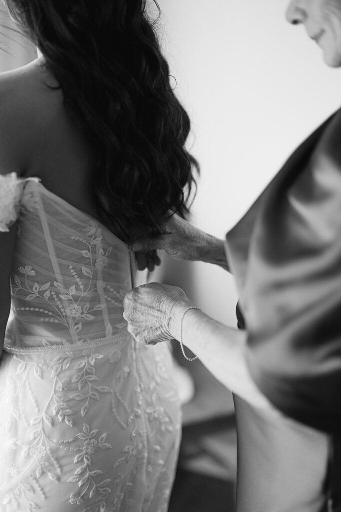 Black and white photo of a bride getting her dress zipped up