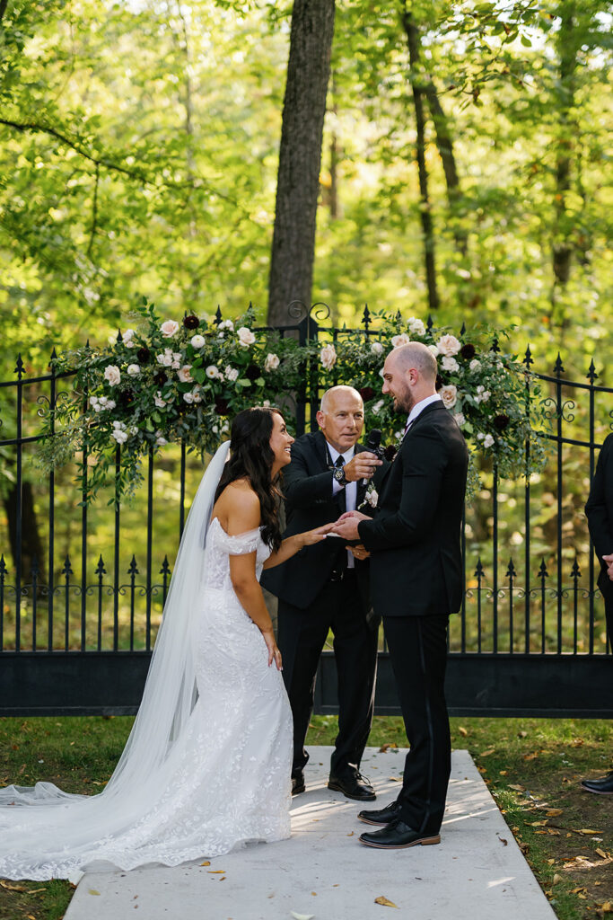 Bride and groom exchanging rings during their outdoor fall Ritz Charles wedding ceremony in Indianapolis, Indiana