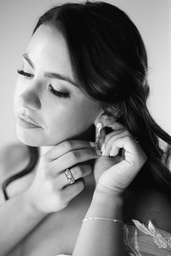 Black and white photo of a bride putting her earrings in