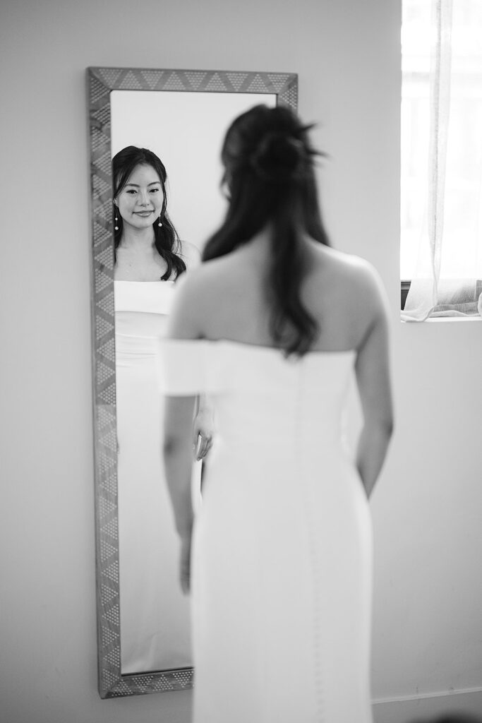 Black and white photo of a bride looking at herself in the mirror