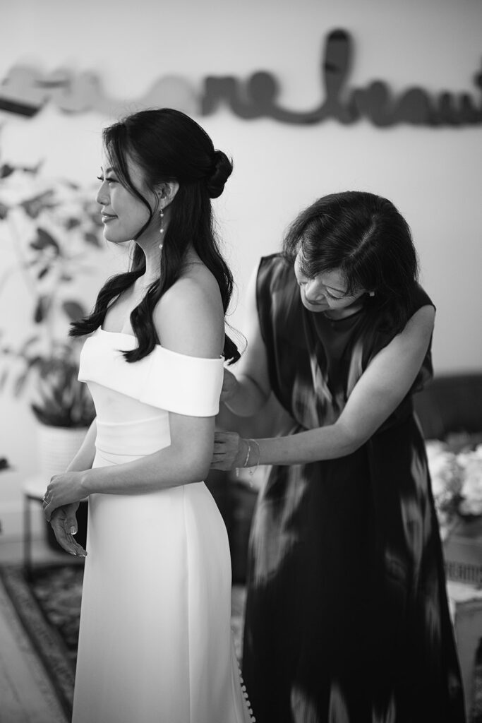 Black and white photo of a bride helping her daughter zip up her dress