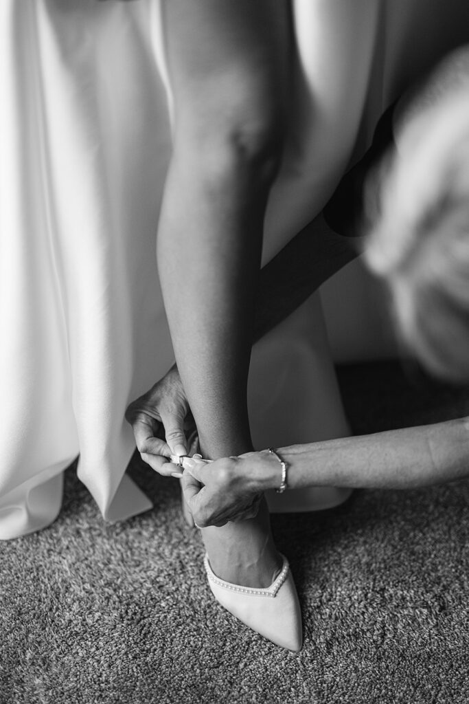 Black and white photo of a bride getting her jewelry put on 