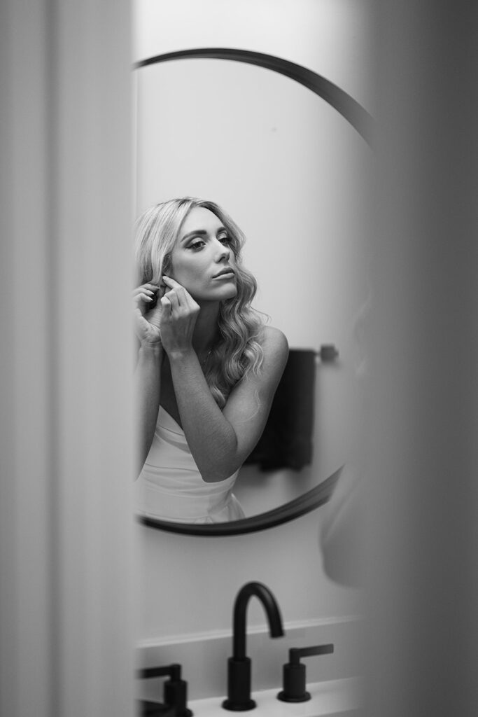 Black and white photo of a bride putting her earrings in