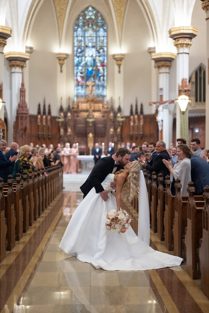 Bride and groom end of the aisle dip kiss during their Immaculate Conception Fort Wayne wedding ceremony