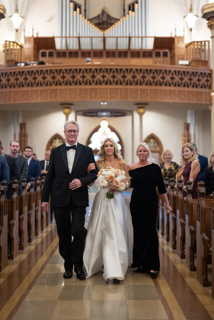 Bride being walked down the aisle by her father and mother