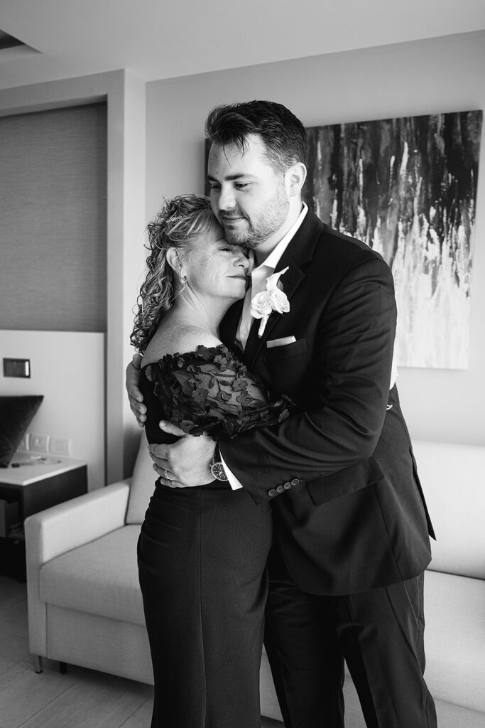 Black and white photo of a groom sharing a first look and hug with his mother