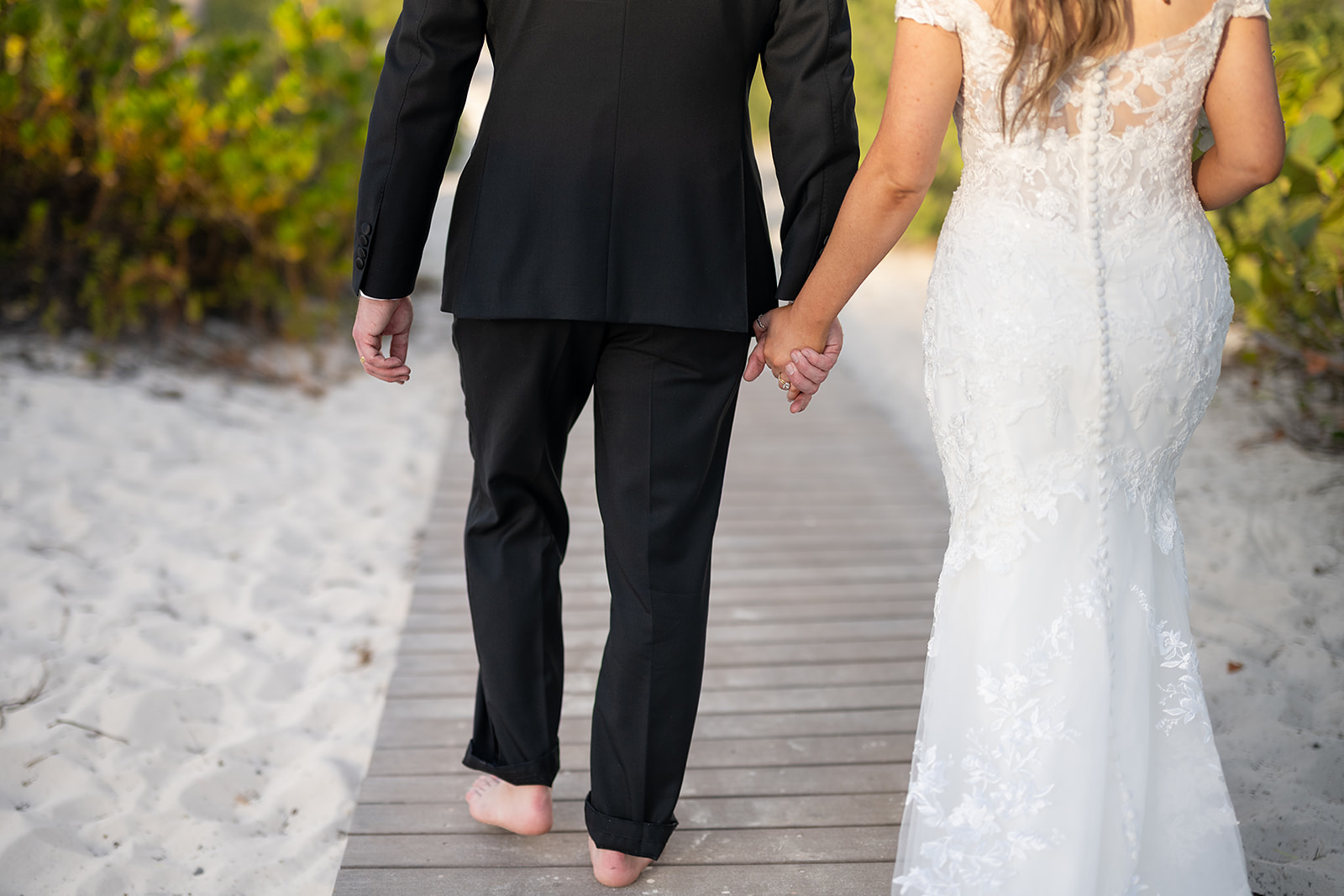 Bride and groom holding hands and walking a beach pathway