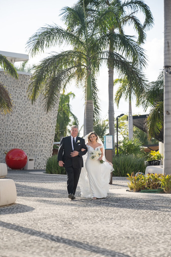 Bride walking down the aisle with her father for her outdoor Grand Palladium Costa Mujeres wedding ceremony at Deck in The Village