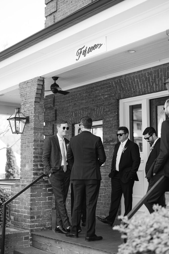 Candid wedding photo of a groom and his groomsmen mingling outside of The Bunn House