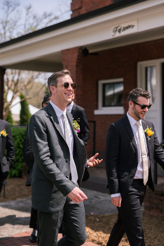 Candid wedding photo of a groom and his groomsmen mingling outside of The Bunn House