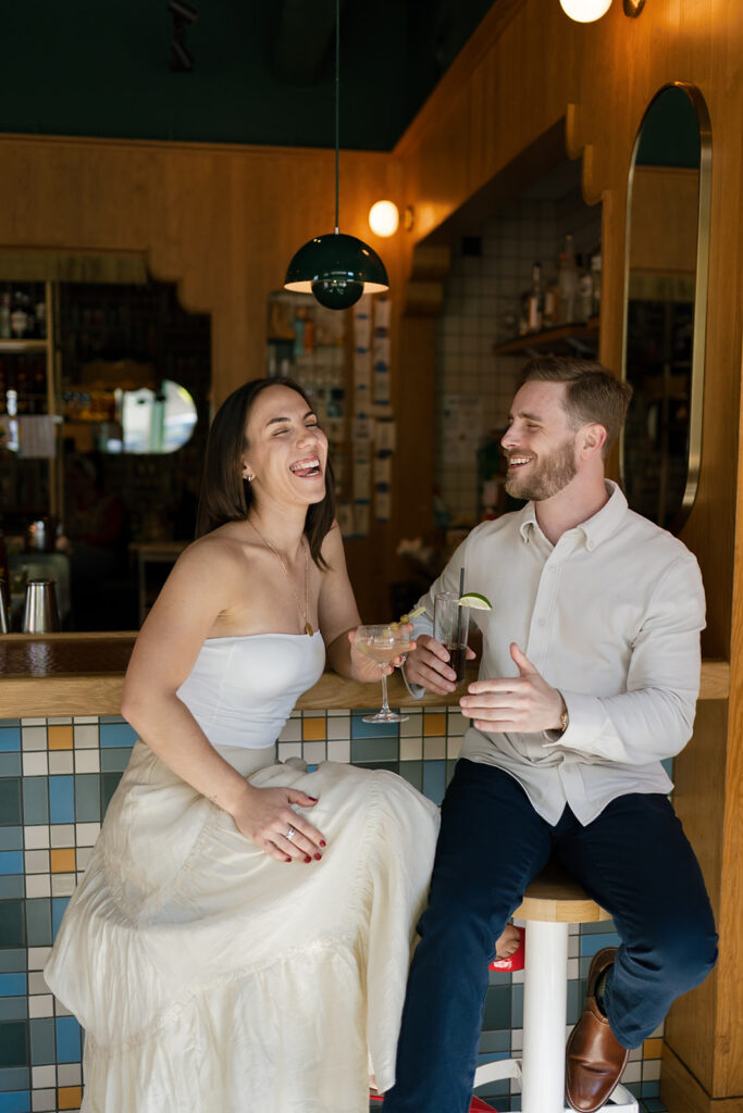 Couple laughing together as they share drinks at a cocktail bar