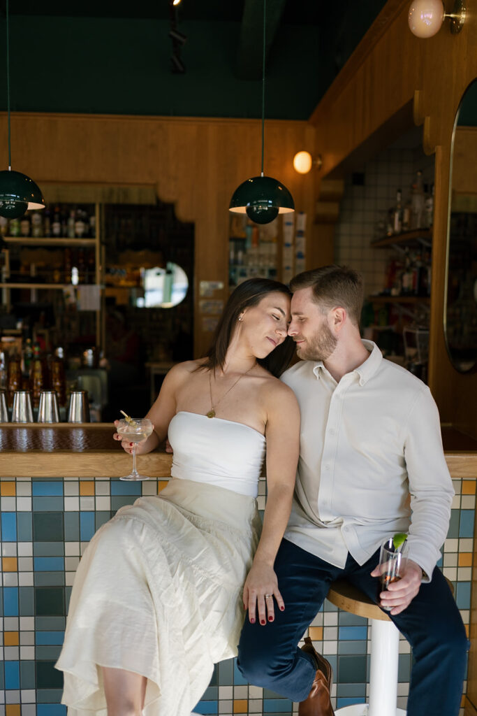Couple cuddled up together at a cocktail bar during their engagement session